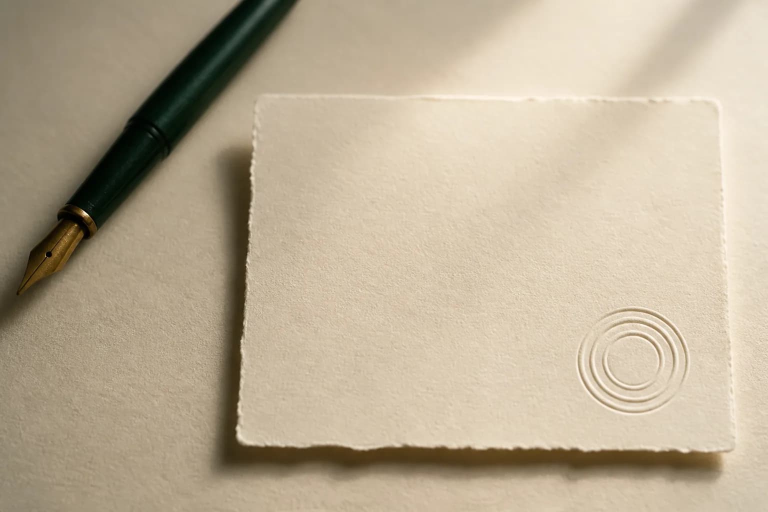 A sheet of heavy deckle-edged paper with a blind-embossed seal, beside a green fountain pen